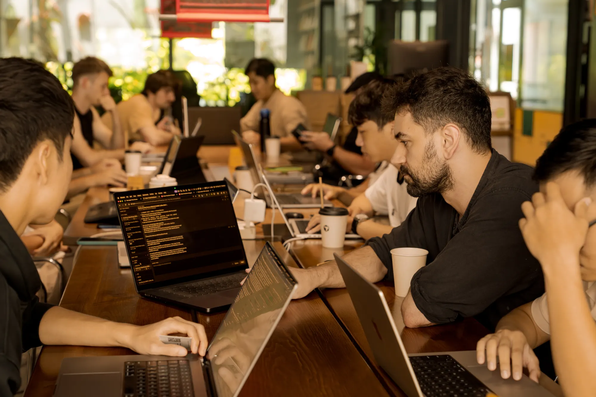 Developers focused on code along a communal table during a Cursor Da Nang coworking session