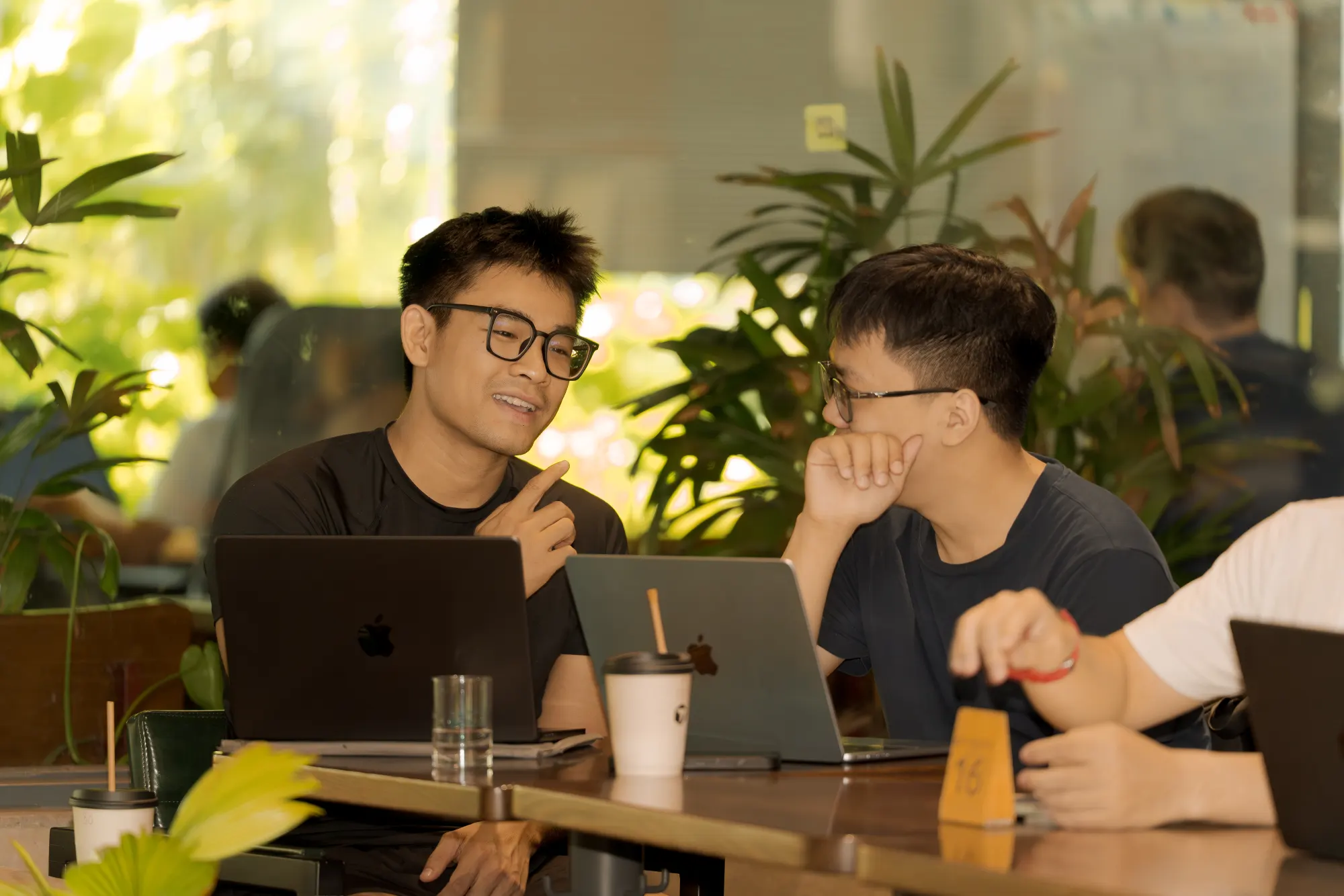 Two developers with MacBooks discussing a project over coffee at a Cursor Da Nang meetup